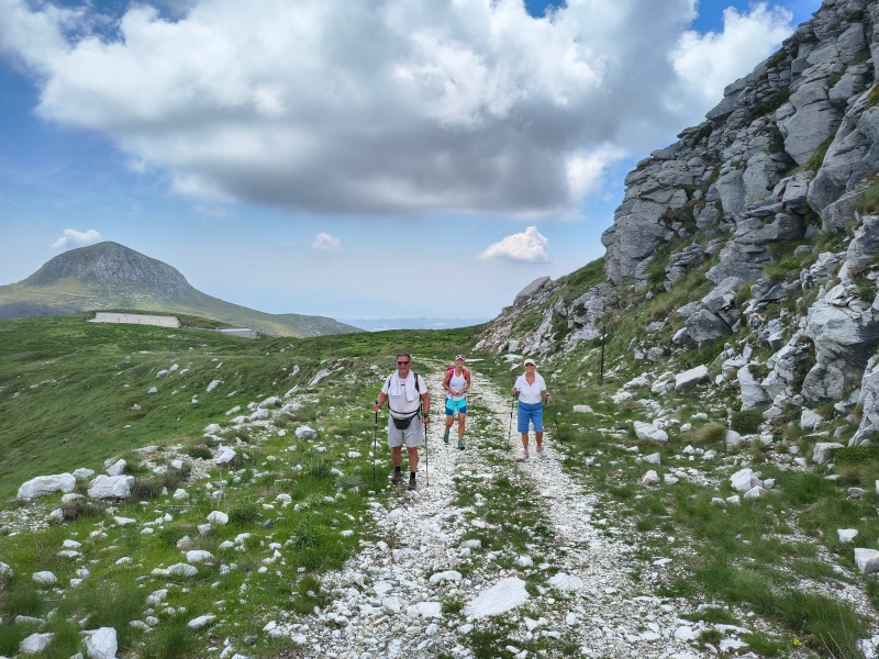 Mehrere Wandernde auf einem steinigen Weg zwischen grünen Berghängen im Pangeon