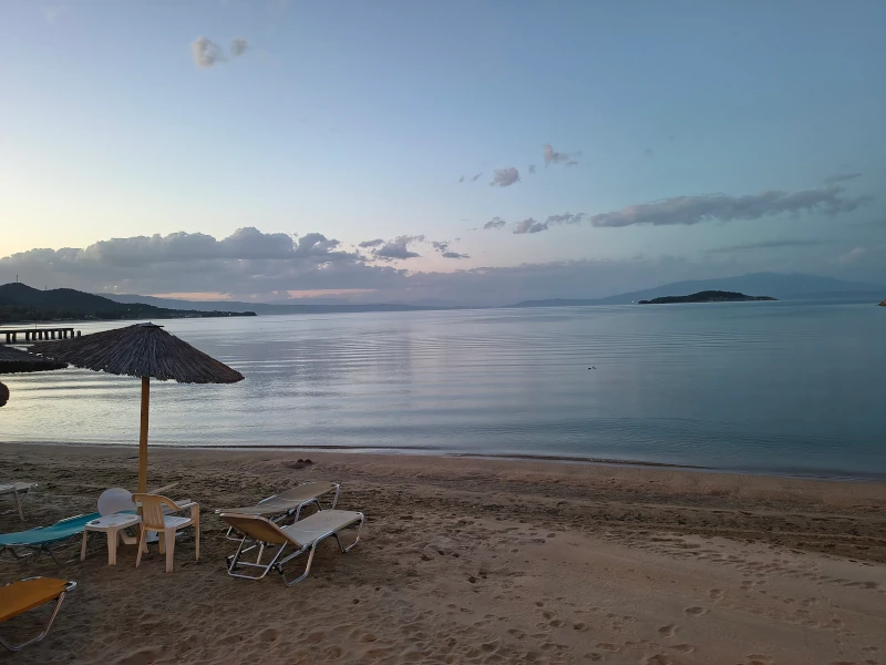 Sonnenschirme und Liegestühle am ruhigen Strand von Olympiada in der Abenddämmerung